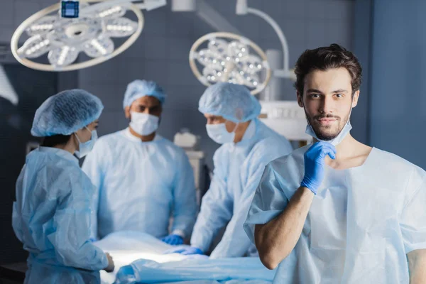 Chirurg, patrząc na kamery z kolegami — Zdjęcie stockowe