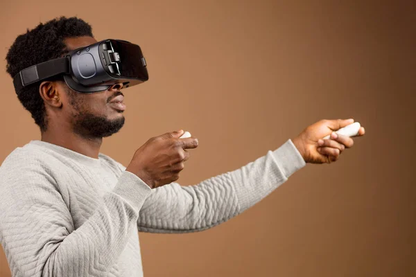 Hombre afroamericano en auriculares de realidad virtual jugando con joystick mientras está sentado en la silla de la bolsa de frijoles —  Fotos de Stock