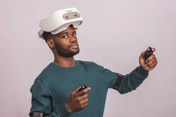 El hombre africano usa gafas de realidad virtual, sostiene controladores de juego, aislado —  Fotos de Stock
