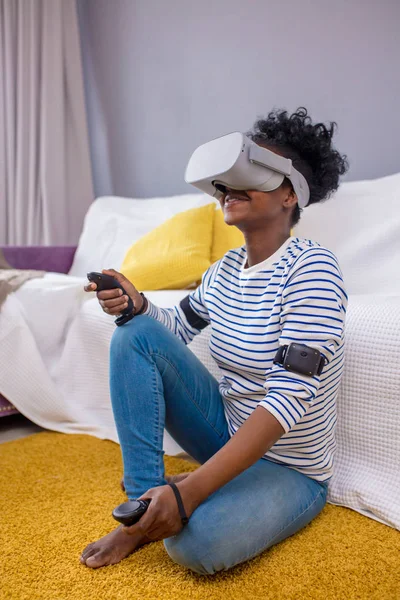 African woman watching video using VR glasses with remote control at home.