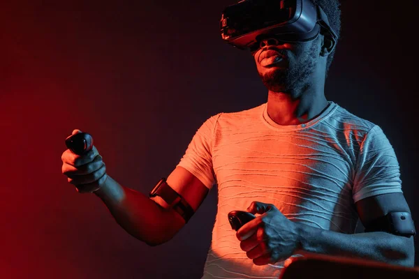 Young man wearing VR headset watching video, isolated on dark red dual light.