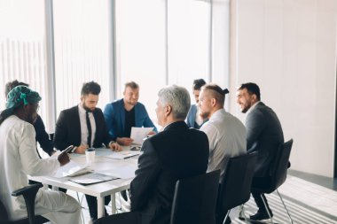 Çok ırklı erkek işletme yöneticileri konferans masasında oturan projeyi tartıştılar