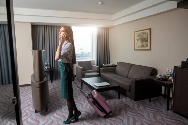 Foto de la joven mujer de negocios sonriente charlando en el teléfono inteligente en el hotel — Foto de Stock