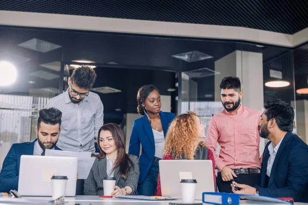 Equipo de trabajo multiétnico joven intercambia ideas reunidas alrededor de computadoras portátiles —  Fotos de Stock