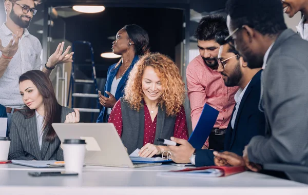 Equipo de trabajo multiétnico joven intercambia ideas reunidas alrededor de computadoras portátiles —  Fotos de Stock