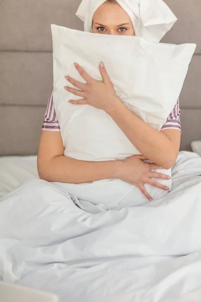 Όμορφη κοπέλα που αγκαλιάζει μαξιλάρι ενώ κάθεται στο κρεβάτι — Φωτογραφία Αρχείου
