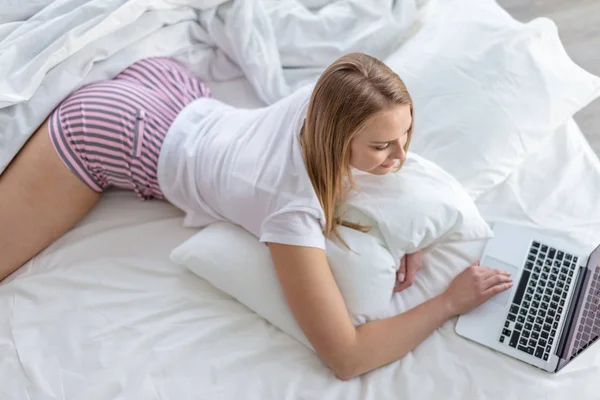 Menina bonito trabalhando no laptop enquanto descansa na cama — Fotografia de Stock