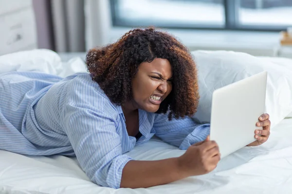 Mujer enojada estresada usando el ordenador portátil mientras está acostado en la cama —  Fotos de Stock