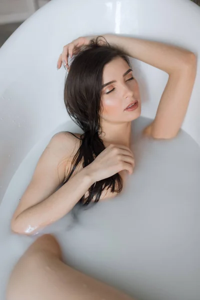Aantrekkelijk meisje met open ogen neemt een bad van melk, het aanraken van haar haren — Stockfoto