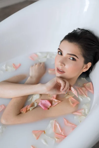 Ung kvinna tar ett mjölkarombad med blomblad — Stockfoto