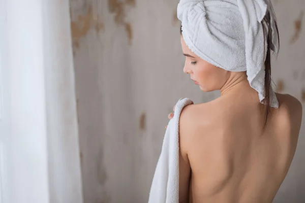 Молода жінка з голим спинкою носить рушник на голові, сидячи на краю ванни . — стокове фото