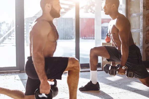 Dos atletas masculinos multirraciales que hacen embestidas con peso en el entrenamiento en interiores — Foto de Stock