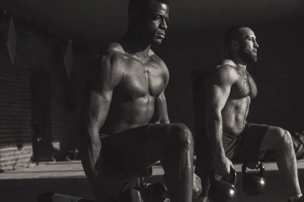 Två raser manliga idrottare att göra utfall med vikt i inomhus träning — Stockfoto