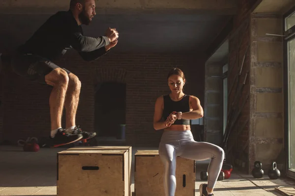 Man and woman jumping tohether on boxes in gym, funcrional workout for people