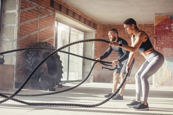Woman and man in gym functional training with battle rope exercising