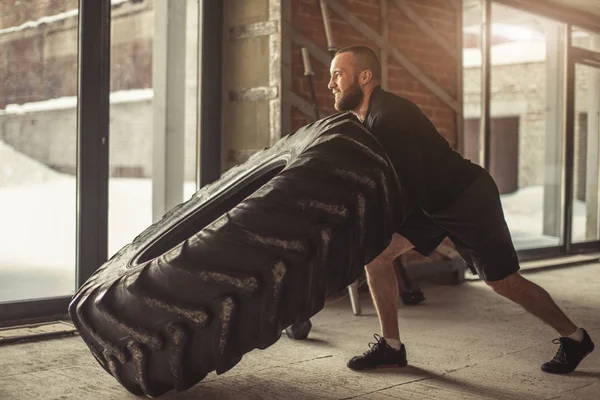 Jovem caucasiano muscular homem lançando pesado pneu no ginásio — Fotografia de Stock