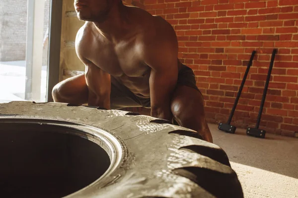 Atletický muž afroamerické cvičení s pneumatikou a koukal v tělocvičně — Stock fotografie