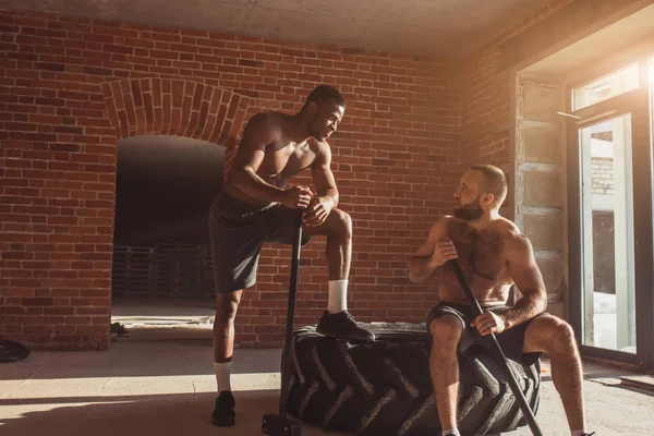 Sport fitness män slår hjul däck med hammare sledge, Cross fit träning. — Stockfoto