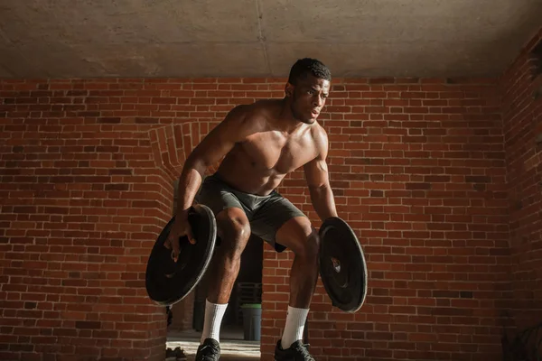 Shirtless african man with barbell plates jumps in air on truck tire in gym — Stock Photo, Image