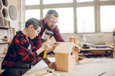 Baba ve oğlu ahşap bir atölyede birlikte çalışıp kuş evi inşa ediyorlar.