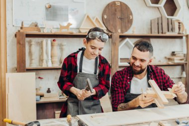 Baba ve oğlu ahşap bir atölyede birlikte çalışıp kuş evi inşa ediyorlar.