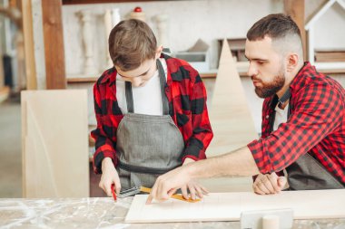 Küçük çocuk, marangoz babasının atölyedeki tahtaları ölçmesine yardım ediyor..