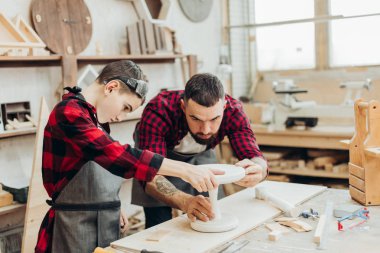 Küçük çocuk, marangoz babasının atölyedeki tahtaları ölçmesine yardım ediyor..