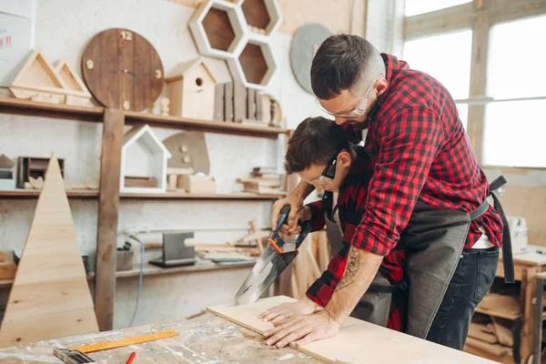 Dad and his son are working in the workshop. They are sawing wooden planks . — Stock Photo, Image