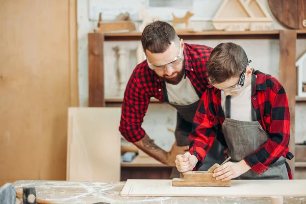 Kaukasische mannelijke timmerman omhelst zijn zoon om vliegtuig te gebruiken tijdens het werken met hout — Stockfoto