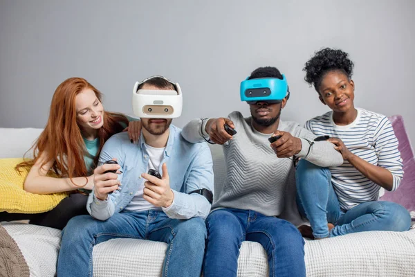 Twee jongens spelen video-games met behulp van Vr bril en vriendinnen steunen hen. — Stockfoto