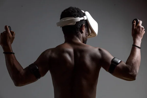 Parte de trás do atleta muscular masculino africano com tronco nu usando fones de ouvido vr — Fotografia de Stock