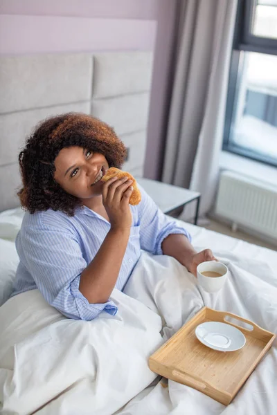 Fundersam lycklig kvinna äter frukost i sängen — Stockfoto