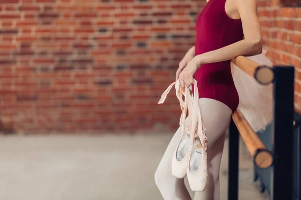 Молодая женщина с пуантами в руках, опирающаяся на балетную стойку — стоковое фото