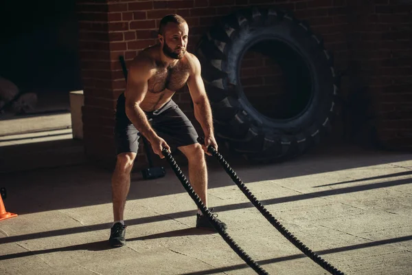 Joven hombre caucásico haciendo ejercicio con cuerdas de batalla en un gimnasio — Foto de Stock