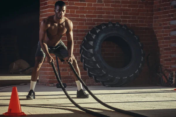 Joven africano entrenando con cuerdas de batalla en un gimnasio — Foto de Stock