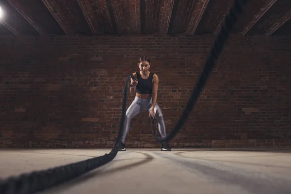 Joven mujer caucásica haciendo ejercicio con cuerdas de batalla en un gimnasio —  Fotos de Stock