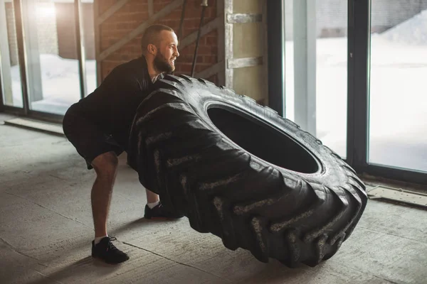 Joven caucásico muscular hombre volteo pesado neumático en gimnasio — Foto de Stock