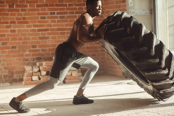 Atletisk afroamerikanska man tränar med däck och tittar bort i gymmet — Stockfoto