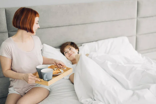 Attrayant fille apportant le petit déjeuner à sa sœur couchée sur le lit — Photo