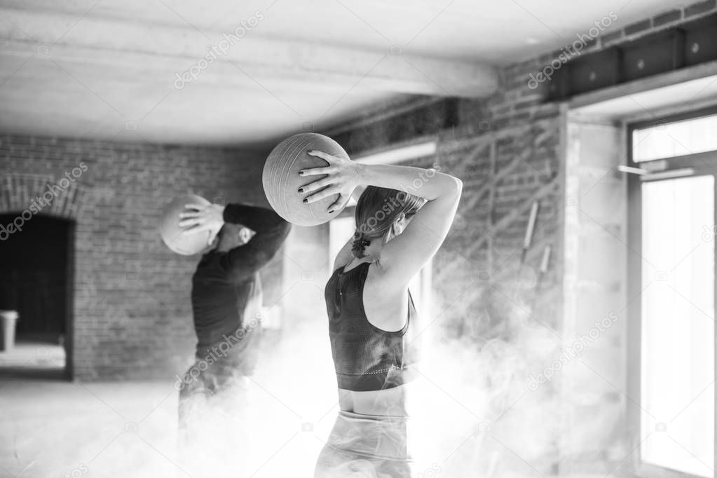 athletic young man and woman in sportswear exercising with medicine balls in gym