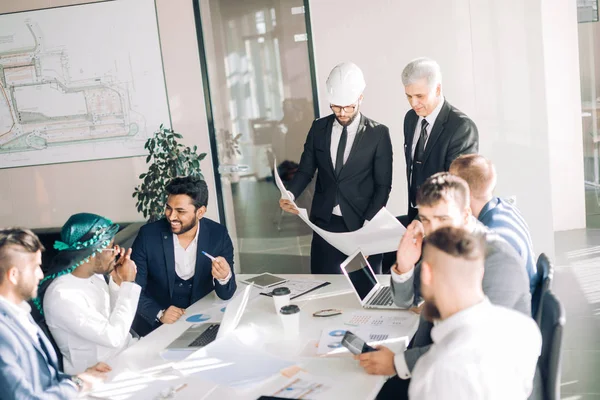 Groupe multiracial de constructeurs et d'architectes discutant du plan au bureau. — Photo