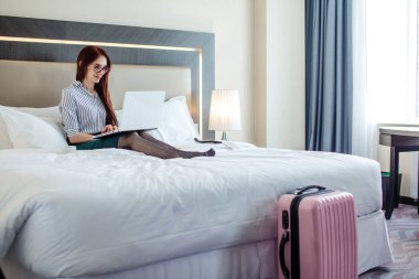 Otel odasında dizüstü bilgisayar ile yatakta yalan zarif kadın giyinmiş.