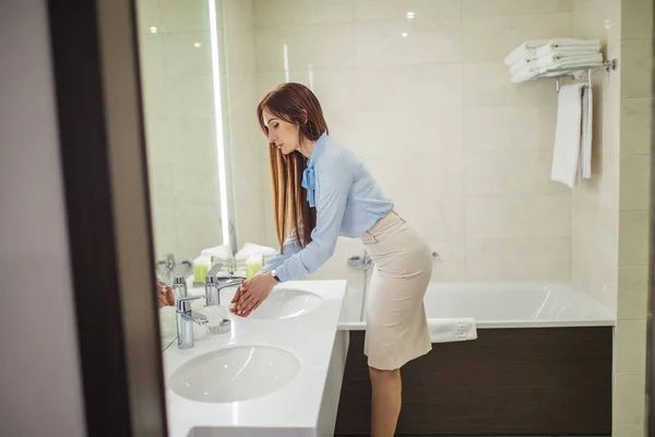 Vacker kvinna i formella slitage tittar på spegeln när du tvättar händerna i badrum — Stockfoto