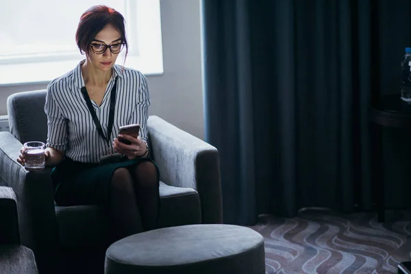 Geschäftsfrau sitzt mit Wasserglas in der Hand im Sessel und telefoniert — Stockfoto