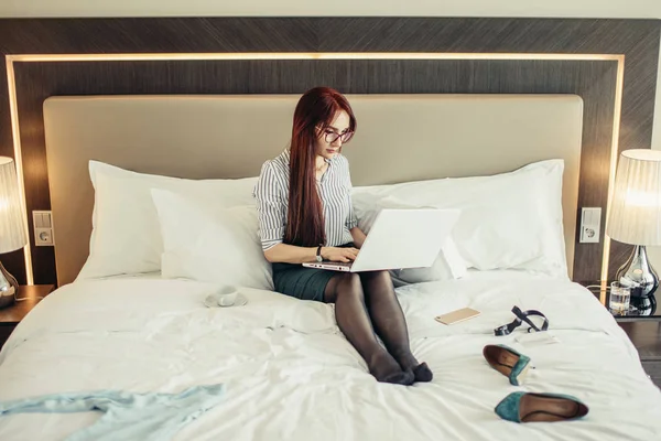 Elegant woman lying dressed on bed with laptop at the hotel room.