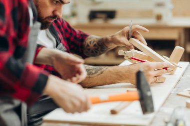 Baba ve oğlu ahşap bir atölyede birlikte çalışıp kuş evi inşa ediyorlar.