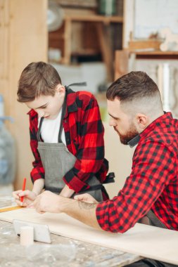 Küçük çocuk, marangoz babasının atölyedeki tahtaları ölçmesine yardım ediyor..