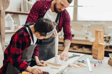 Küçük çocuk, marangoz babasının atölyedeki tahtaları ölçmesine yardım ediyor..