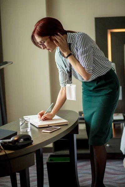 Diseñadora femenina pelirroja que observa detalles del trabajo durante la conversación telefónica . — Foto de Stock