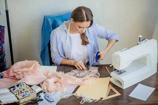 Bonito focado jovem designer de moda cortando tecido de renda rosa na oficina — Fotografia de Stock